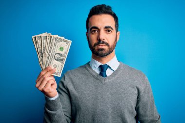 Sakallı, mavi arka planda banknotlar tutan yakışıklı genç bir adam. Zeki bir yüz ifadesi var ve ciddi düşünüyor.
