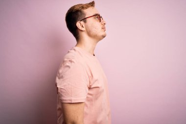 Genç, yakışıklı, günlük tişört giyen, pembe arka planda duran rahat bir görünüm ve kendine güvenen bir gülümseme takınan kızıl saçlı bir adam..