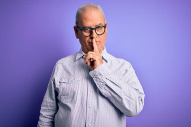 Orta yaşlı, beyaz, çizgili gömlek ve mor arka planda gözlük takan yakışıklı adam sessiz olmak istiyor. Sessizlik ve gizli konsept.