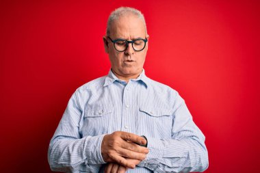 Orta yaşlı yakışıklı, beyaz gömlekli, kırmızı arka planda gözlüklü, rahat ve kendinden emin bir adam.