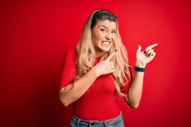 Genç, güzel, sarışın bir kadın, gündelik tişört giyiyor, kırmızı arka planda dikiliyor. Endişeli ve gergin, endişeli ve şaşırmış bir ifadeye işaret ediyor.