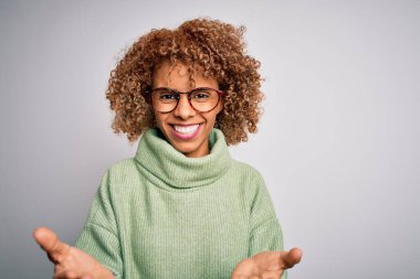 Güzel Afrikalı Amerikalı kadın balıkçı yaka kazak ve gözlük takıyor. Neşeli gülümsüyor ve kollarını açıyor. Hoş geldin, olumlu ve kendinden emin selamlar.