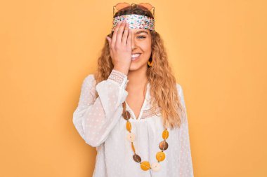 Mavi gözlü, güneş gözlüğü ve aksesuar takan genç, güzel sarışın hippi kadın bir gözünü elinle kapatıyor, yüzünde kendine güvenen bir gülümseme ve şaşırtıcı bir duygu var..