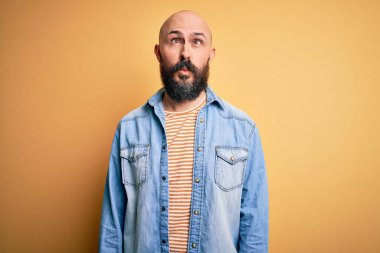 Sıradan kot ceket ve çizgili tişört giyen sakallı yakışıklı kel adam dudaklı balık suratı yapıyor, çılgınca ve komik bir jest. Komik ifade.