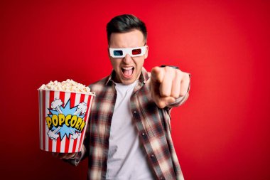 3 boyutlu film gözlüğü takan ve patlamış mısır yiyen yakışıklı beyaz adam kameraya kızgın ve sinirli bir şekilde bakıyor.
