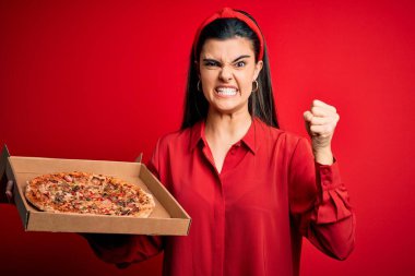 Genç, güzel esmer kadın elinde İtalyan pizzasıyla kırmızı zemin üzerinde teslimat kutusunu tutarken sinirlenmiş ve hayal kırıklığına uğramış öfkeyle bağırıyor, çıldırmış ve el kaldırarak bağırıyor.