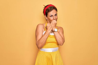 Orta yaşlı, son sınıf rozetli, 50 'li yaşlarda, sarı arka planda eski moda elbise giyen, kavgaya hazır, kızgın ve üzgün yüzlü, sorunlardan korkan bir kadın.