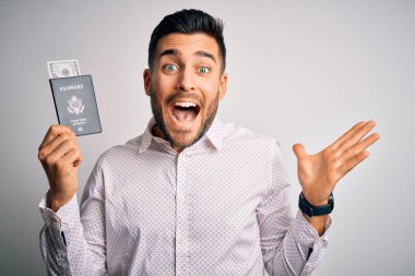 Amerika Birleşik Devletleri pasaportlu genç yakışıklı turist çok mutlu ve heyecanlı, kazanan yüz ifadesi zaferi büyük bir gülümsemeyle kutluyor ve ellerini kaldırıyor.