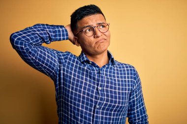 Sarı arka plan üzerine gündelik tişört ve gözlük takan genç, yakışıklı latin adam soru sormayı merak ediyor. Şüpheyle kararsız, kafa kafaya düşünerek. Düşünceli kavram.