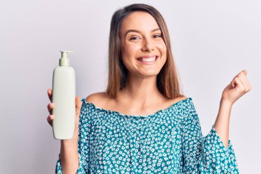 Genç ve güzel bir kız elinde krem losyon şişesiyle gururla bağırıyor, zaferi kutluyor ve başarıyı kollarını kaldırarak kutluyor. 