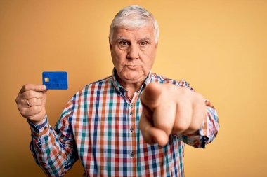 Ödemeyi finanse etmek için kredi kartı tutan kıdemli beyaz müşteri kamerayı işaret ediyor ve sen, el işareti, ön taraftan pozitif ve kendinden emin bir jest.