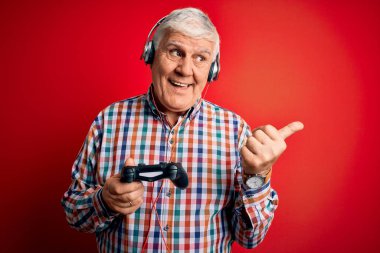 Kıdemli yakışıklı, ağarmış oyuncu oyun oynuyor. Oyun çubuğu ve kulaklık takıyor. Baş parmağınla işaret ediyor ve gülümsüyor.