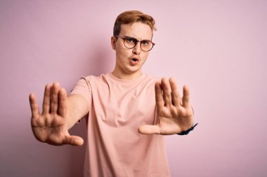Genç, yakışıklı, günlük tişört giyen, pembe arka planda duran, el hareketlerini durduran, sinirli ve hayal kırıklığına uğramış bir adam.