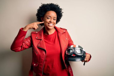 Kıvırcık saçlı, motosiklet kasklı, neşeli gülümseyen ve parmaklarını, dişlerini ve ağzını gösteren Afro-Amerikan motosikletli genç bir kadın. Diş sağlığı konsepti.