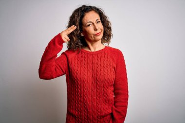 Orta yaşlı esmer kadın izole edilmiş beyaz arka planda dikilmiş silah gibi el ve parmakları işaret ederek kendini vuruyor, intihar hareketi yapıyor..