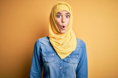 İslami tesettüre bürünmüş genç ve güzel bir kız. Sarı arka planda duruyor. Şaşırmış ve korkmuş bir ifade, korku ve heyecanlı bir yüz..