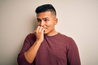 İzole edilmiş beyaz arka planda dikilen gündelik süveter giyen genç ve yakışıklı Latin adam elleri ağız yiyen tırnaklarla stresli ve gergin görünüyor. Endişe sorunu.