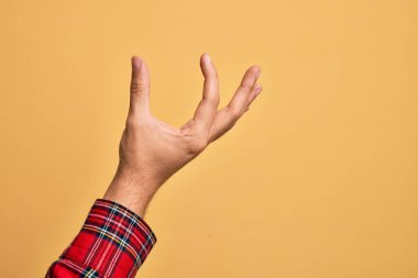 İzole edilmiş sarı arka plan üzerinde parmaklarını gösteren beyaz bir adamın eli. Görünmez bir şeyi alıp, parmaklarıyla uzayı gösteren bir nesneyi tutuyor.