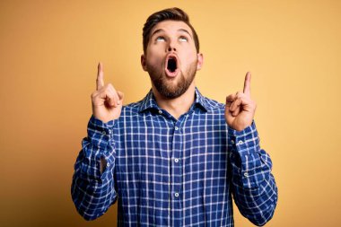 Sarışın, sakallı ve mavi gözlü genç işadamı sarı arka planda tişört giyiyordu. Şaşırmış ve şaşırmıştı. Parmaklarıyla işaret ediyor ve kollarını kaldırıyordu..
