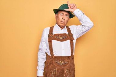 Sarı arka planda Alman geleneksel Ekim Festivali kıyafeti giyen yaşlı, gri saçlı adam. Alnında parmakları olan insanlarla alay ediyor. Ezik hareketler yapıyor, alay ediyor ve hakaret ediyor..