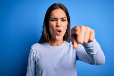 Genç, güzel, esmer, sıradan bir süveter giyen, mavi arka planda duran bir kadın. Kameraya kızgın ve sinirli olduğunu gösteriyor.