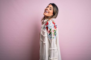 Moda kıyafetleri giyen genç ve güzel bir kadın. Manken, sokak tarzı giyiniyor. Pembe arka planda dikiliyor.