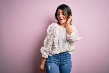 Moda kıyafetleri giyen genç ve güzel bir kadın. Manken, sokak tarzı giyiniyor. Pembe arka planda dikiliyor.