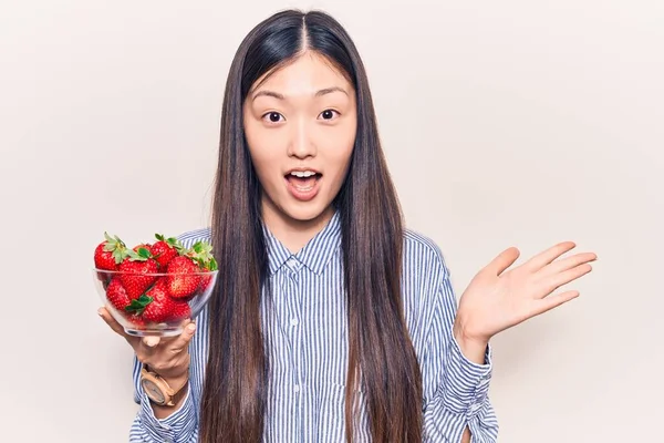 年轻美丽的中国女人举着一碗草莓 笑容满面 高举双手庆祝胜利 — 图库照片