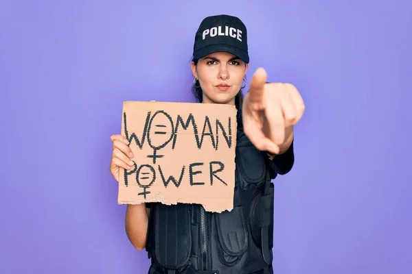 Police woman wearing security bulletproof vest uniform holding woman power protest cardboard pointing with finger to the camera and to you, hand sign, positive and confident gesture from the front