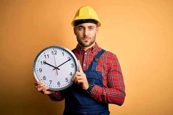 Junger Bauarbeiter Mit Schutzhelm Und Großer Uhr Auf Gelbem Hintergrund — Stockfoto