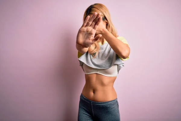 Young beautiful blonde sportswoman doing sport wearing sportswear over pink background covering eyes with hands and doing stop gesture with sad and fear expression. Embarrassed and negative concept.