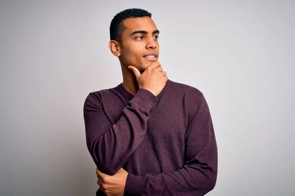 Young handsome african american man wearing casual sweater over white background with hand on chin thinking about question, pensive expression. Smiling with thoughtful face. Doubt concept.