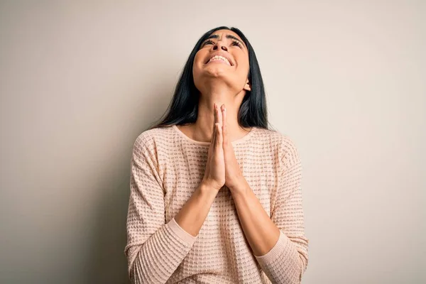 Young beautiful hispanic woman wearing elegant pink sweater over isolated background begging and praying with hands together with hope expression on face very emotional and worried. Begging.