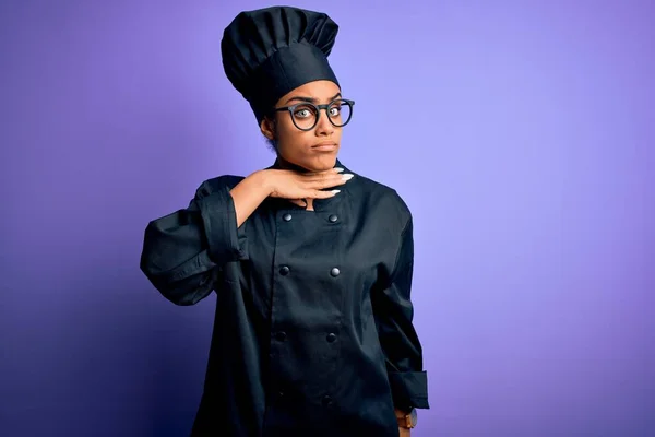Young african american chef girl wearing cooker uniform and hat over purple background cutting throat with hand as knife, threaten aggression with furious violence