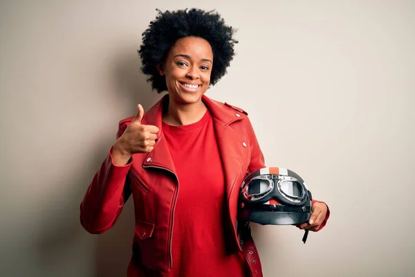 巻き毛を持つ若いアフリカ系アメリカ人のアフロバイクの女性は手で幸せな親指アップジェスチャーを行うオートバイのヘルメットを保持しています 成功を示すカメラを見て表現を承認する — ストック写真