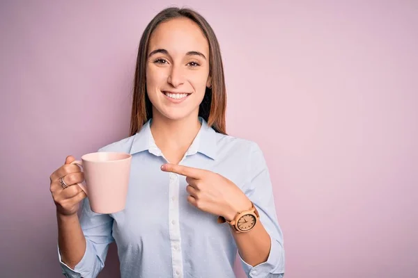 年轻美丽的女人站在孤立的粉色背景上喝着一大杯咖啡 她非常高兴地用手和手指指点着 — 图库照片