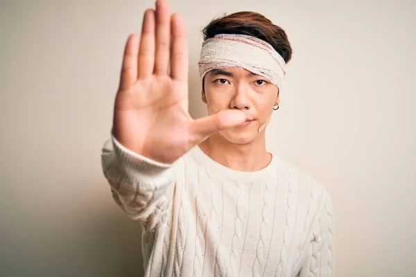 若いハンサムな中国人男性が手の手のひらで歌うのを停止する頭の上に包帯やストリップを身に着けて事故で負傷した 顔に負と深刻なジェスチャーで警告式 — ストック写真