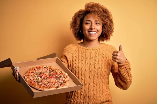 若いですアフリカ系アメリカ人アフロ女性とともに巻き毛保持デリバリーボックスでイタリアの新鮮なピザ幸せなです大きな笑顔でやってOkサイン 指で親指アップ 優れたサイン — ストック写真