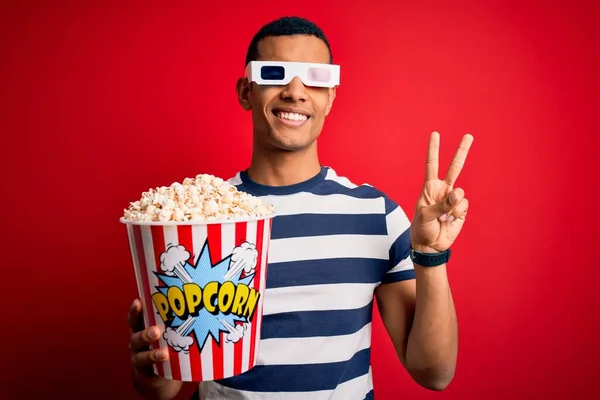 年轻英俊的非洲裔美国人 拿着3D眼镜看电影 吃着爆米花 开心地微笑着 用手指在镜头前眨眼示意胜利 第二点 — 图库照片