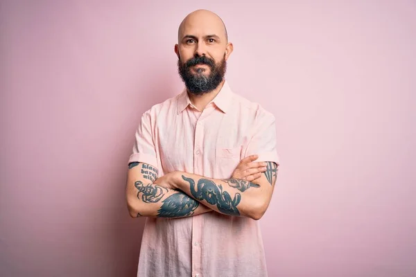 Handsome bald man with beard and tattoo wearing casual shirt over isolated pink background happy face smiling with crossed arms looking at the camera. Positive person.