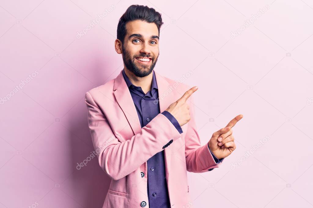 Young handsome man with beard wearing elegant jacket smiling and looking at the camera pointing with two hands and fingers to the side. 