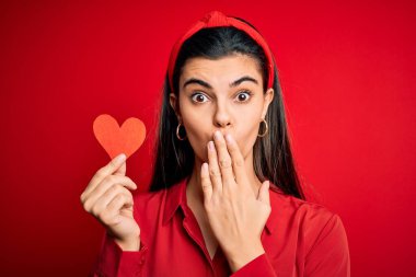 Genç, güzel, esmer, romantik bir kadın elinde sevgililer günü için kırmızı kalp kâğıdı, ağzı kapalı, utancından ağzı açık, korkunun ifadesi, sessizlikten korkan, gizli bir konsept.