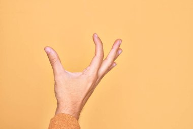 İzole edilmiş sarı arka plan üzerinde parmaklarını gösteren beyaz bir adamın eli. Görünmez bir şeyi alıp, parmaklarıyla uzayı gösteren bir nesneyi tutuyor.