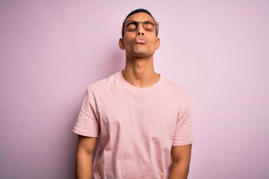 Yakışıklı Afro-Amerikan erkeği pembe arka plan üzerinde günlük tişört ve gözlük takıyor ve kameraya bakıp güzel ve seksi bir öpücük yolluyor. Aşk ifadesi.