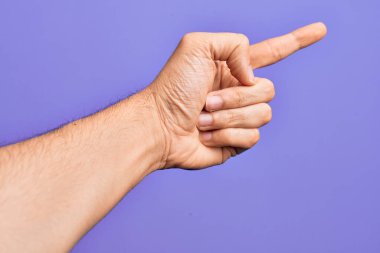 İzole edilmiş mor arka plan üzerinde parmaklarını gösteren beyaz bir gencin eli işaret parmağıyla kenarı işaret ediyor ve bir seçim yapıyor.
