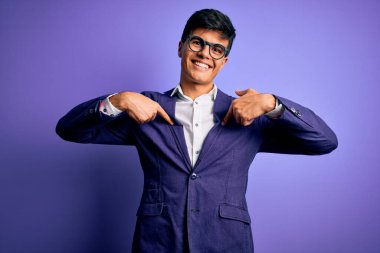 Ceket ve gözlük takan yakışıklı genç bir iş adamı. Mor arka planda, kendine güvenen, yüzünde bir gülümseme, kendini gururla ve mutlu bir şekilde gösteren biri..