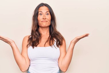 Genç, güzel, esmer, günlük tişört giyen bir kadın izole edilmiş beyaz arka planda dikiliyor. Kameraya gülümsüyor ve zafer işareti yapıyor. İki numara..