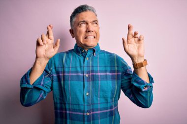 Orta yaşlı, yakışıklı, gri saçlı, sıradan bir gömlek giyen, pembe arka planda yaşayan, umut ve gözlerin kapalı bir şekilde gülümseyen bir adam. Şans ve batıl inanç..