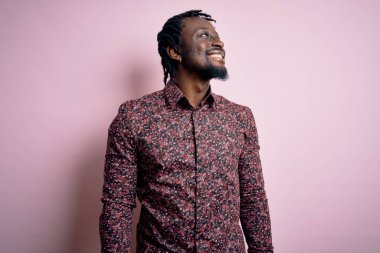 Genç, yakışıklı, Afro-Amerikalı bir adam pembe arka planda dikilmiş, yüzünde gülümseme, doğal bir ifade ile diğer tarafa bakıyor. Kendinden emin gülen.