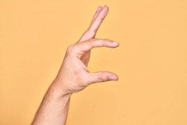 İzole edilmiş sarı arka plan üzerinde parmaklarını gösteren beyaz bir adamın eli. Görünmez bir şeyi alıp, parmaklarıyla uzayı gösteren bir nesneyi tutuyor.